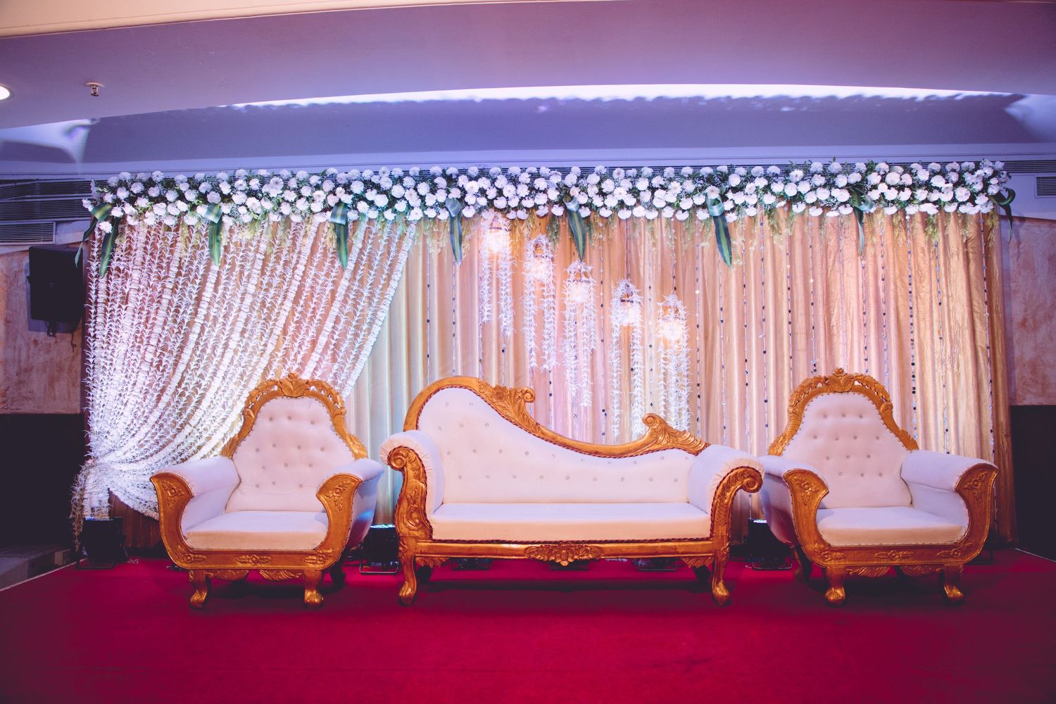 Elegant wedding stage setup with white floral backdrop and vintage style seating.