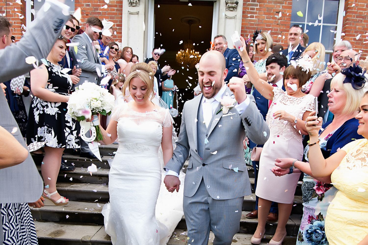 Newlyweds exit church steps while guests shower them with confetti.
