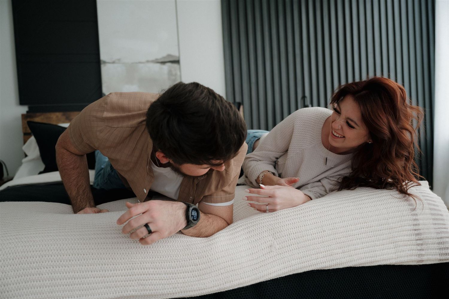 Couple sharing playful moments while lying on white bedding in a modern bedroom.