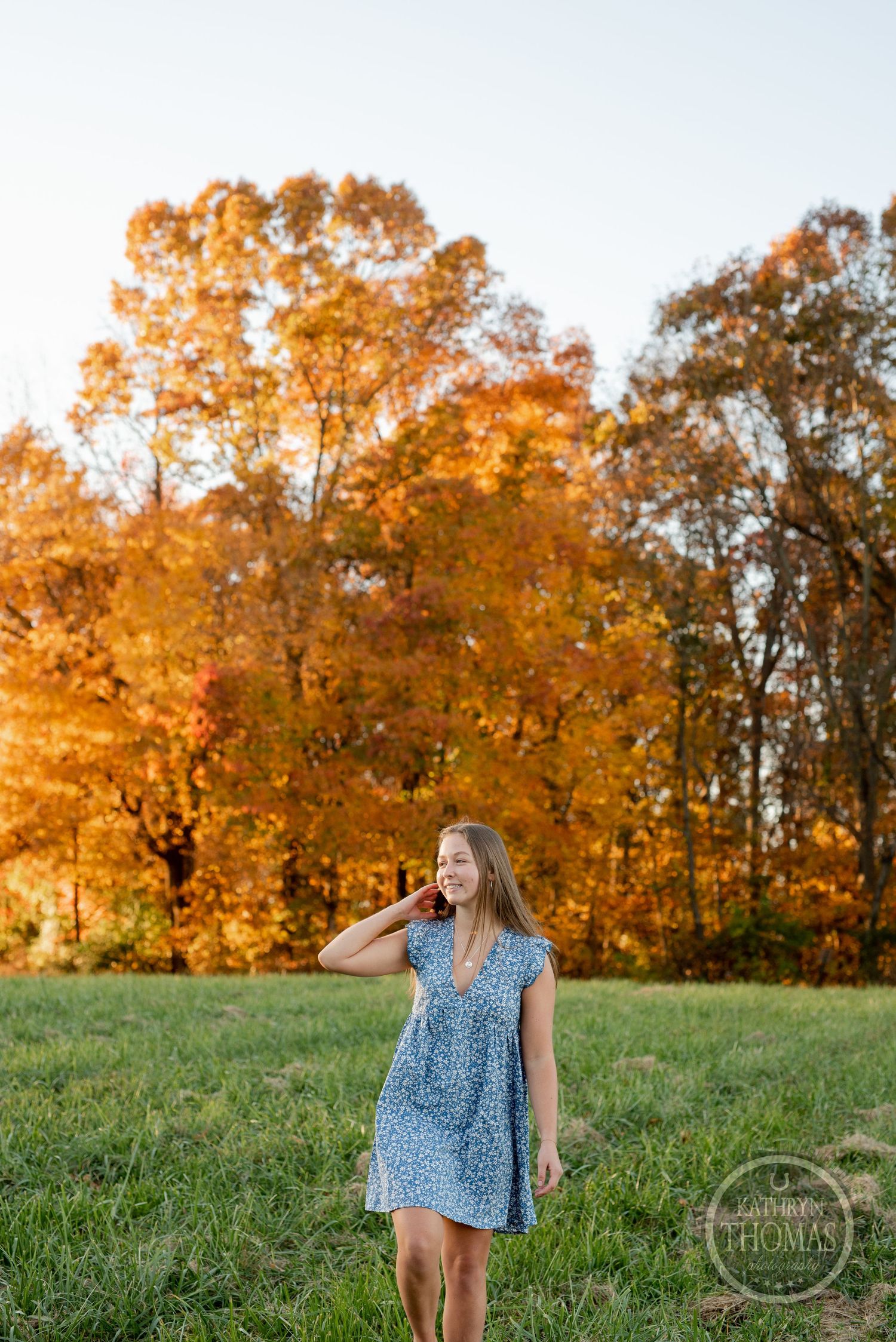 A blue floral dress stands out against vibrant orange autumn trees during sunset.