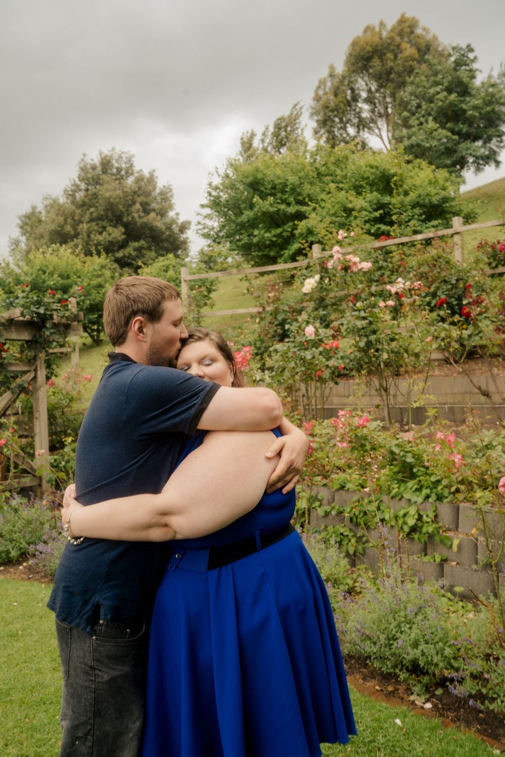 PLus size couple dressed in blue embrace after proposal in rose garden