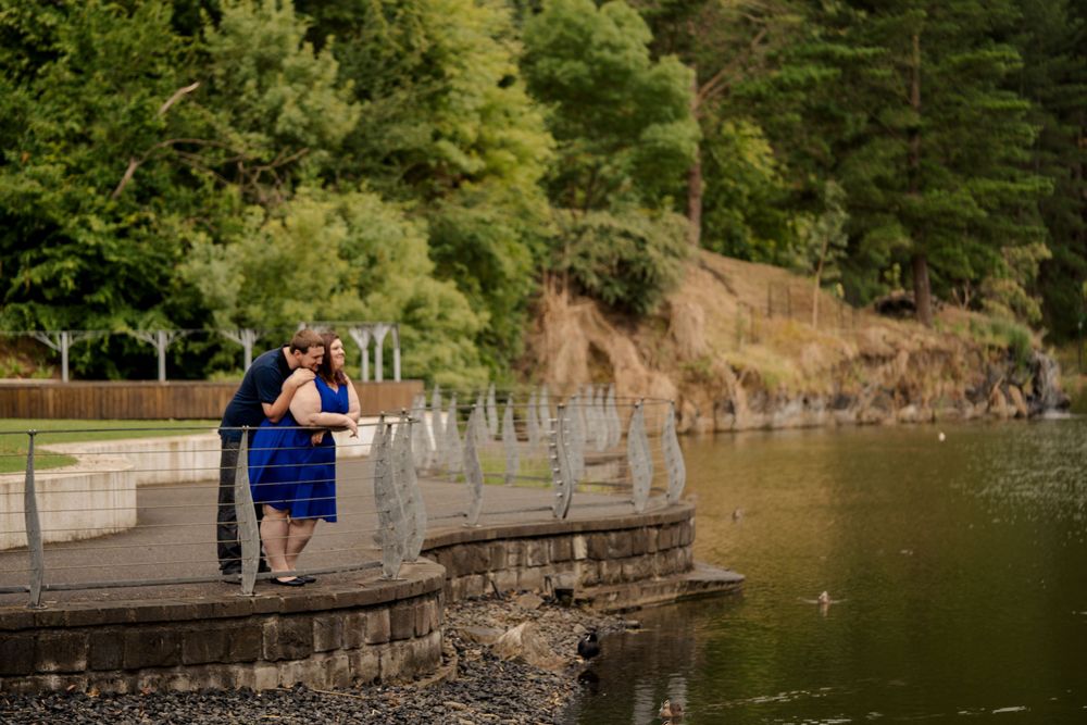 newly engaged plus size couple dressed in blue enjoying scenic view over lake