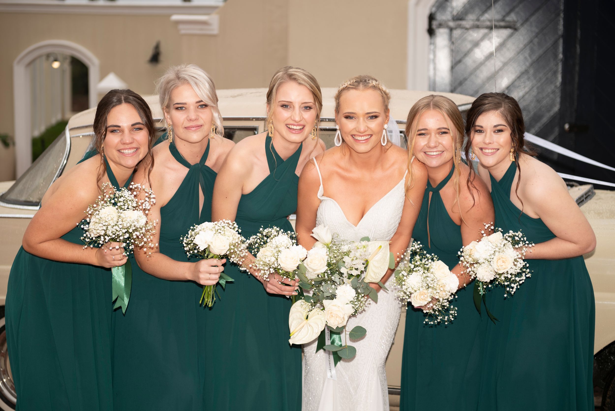 Wedding party wearing emerald green dresses poses with bouquets of white flowers.