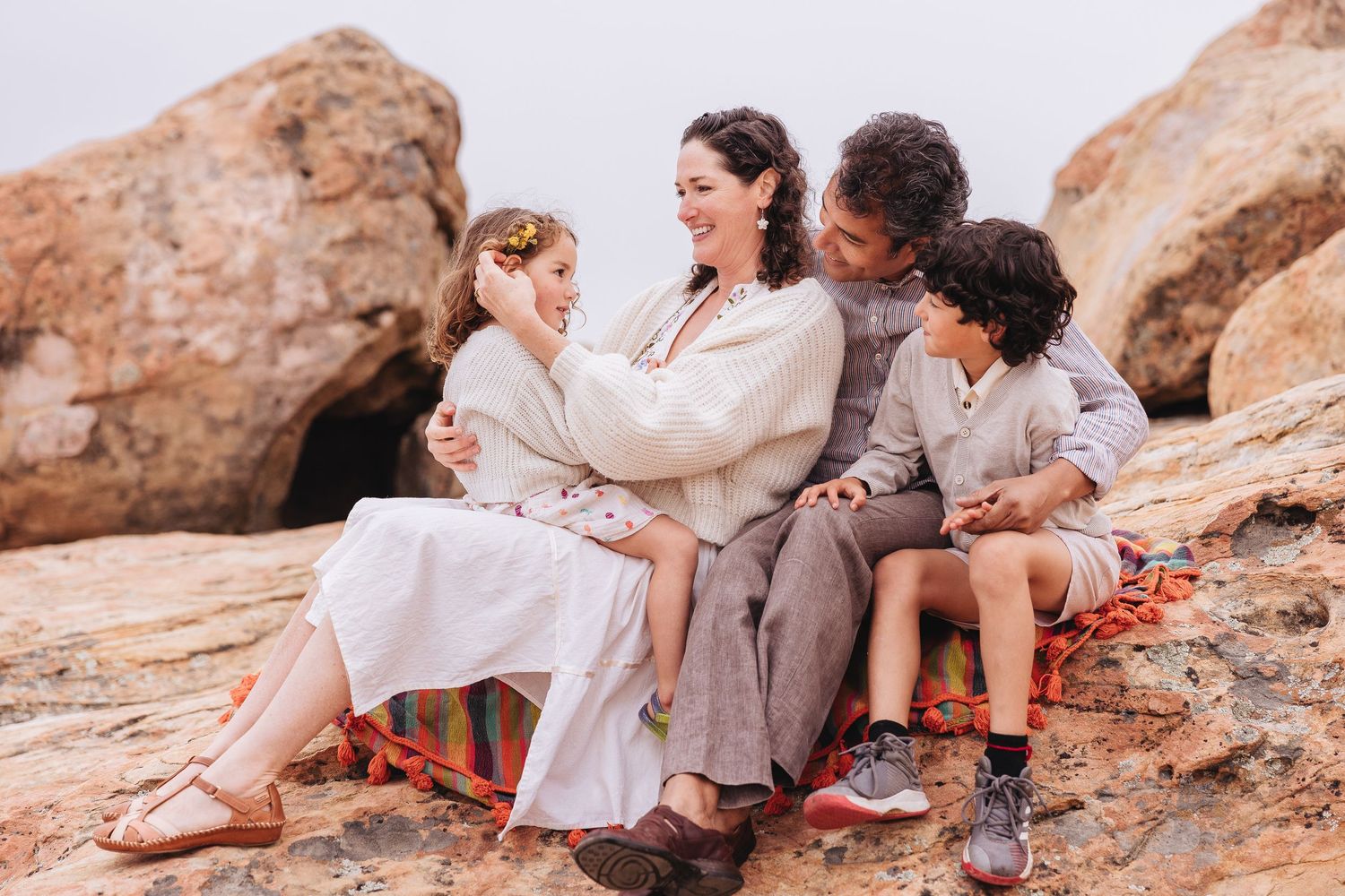 Group sitting on rocky beach outcrop during sunset.