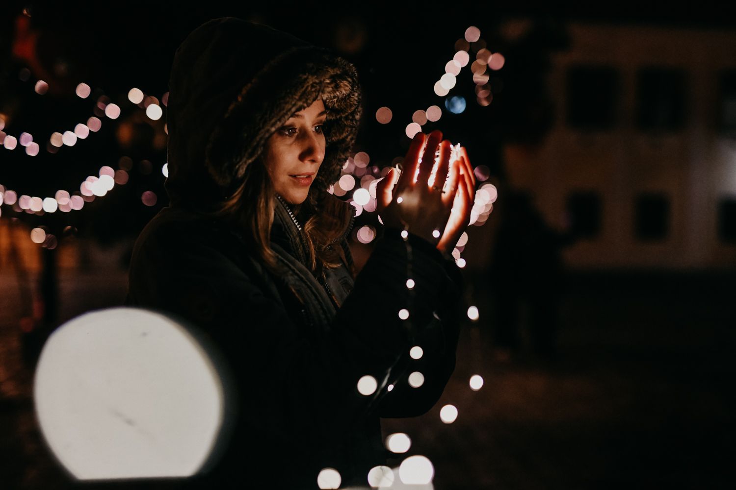 A silhouetted figure stands against blurred bokeh lights in a dark nighttime scene.