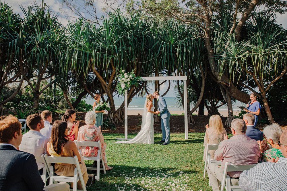 Bride and groom kissing under the arbour in front of wedding crowd at Noosa wedding