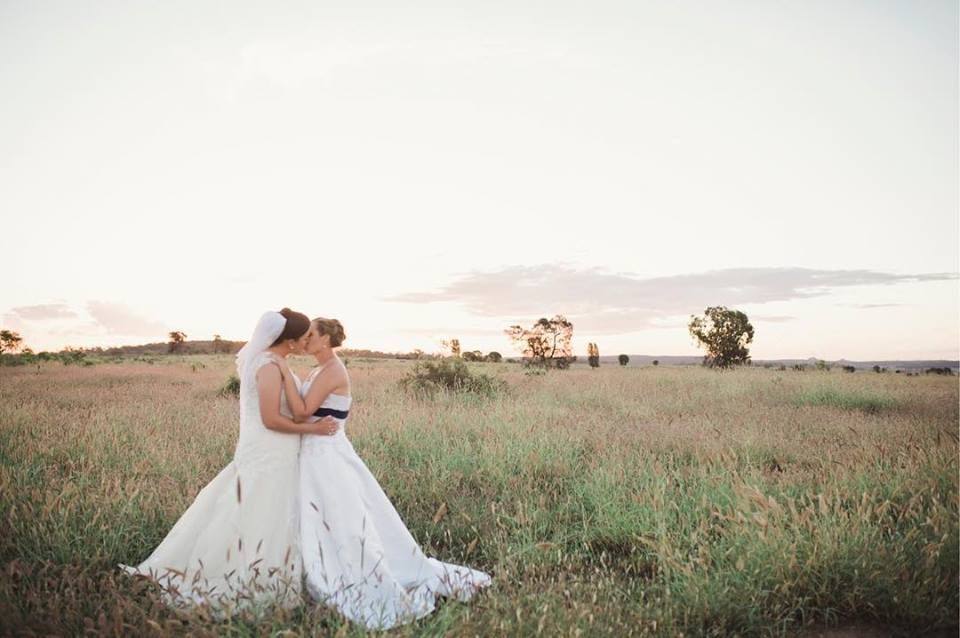 Two brides kissing in a field on sunset