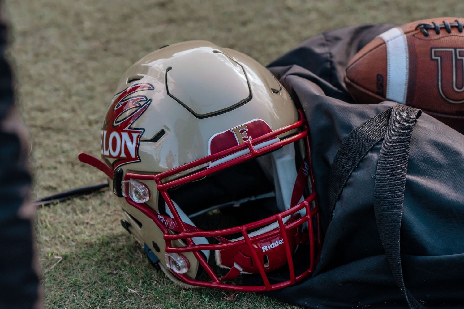 Red and gold football helmet with lion mascot logo rests on field during game day.