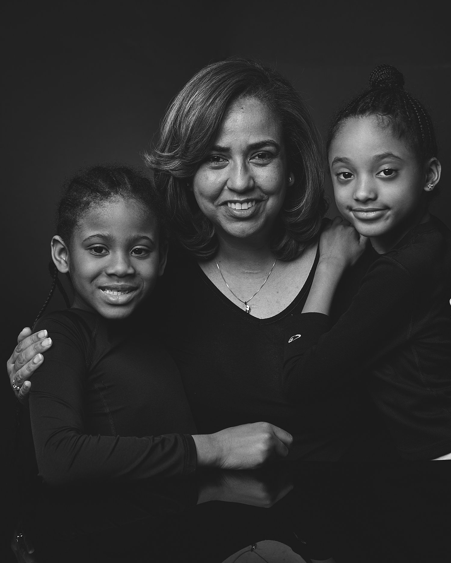 Black and white studio portrait of a mother smiling with two young daughters in matching outfits.