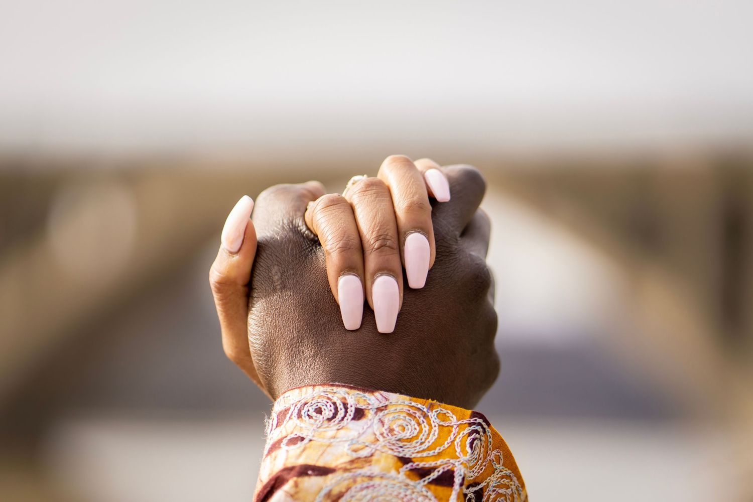 Close-up of manicured hands with pink nails clasped together against a blurred background.