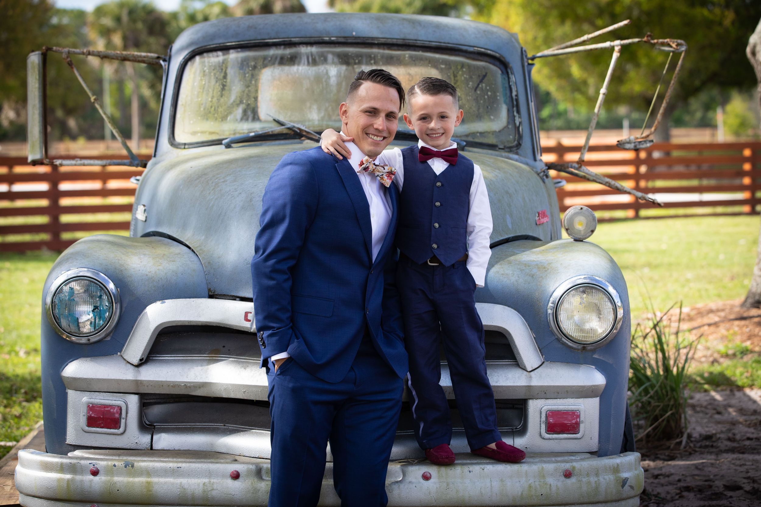 Vintage blue Chevrolet pickup truck serves as rustic backdrop for wedding photo at rural venue.