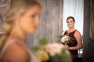 Bridesmaid in burgundy dress holds flower bouquet in rustic wood-paneled room.