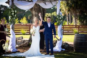 Ceremony under white draped arch with wine barrels and wooden fence backdrop.
