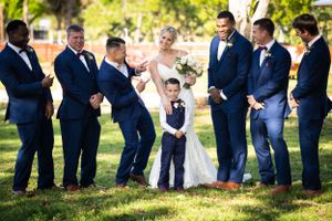 Wedding party shares a lighthearted moment on the lawn in navy blue suits.