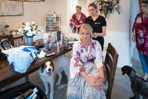 Wedding preparation scene with white dog and floral arrangements on wooden table.