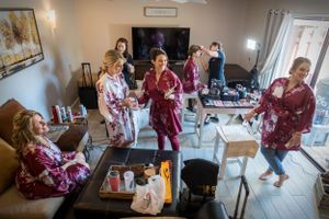 Wedding party getting ready in burgundy robes in cozy living room setting.