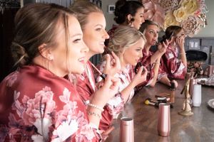 Bridal party in matching burgundy robes enjoying drinks and laughing at a bar counter.