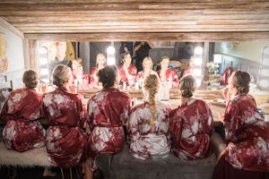 Wedding party in matching robes sits at illuminated makeup counter during preparations.