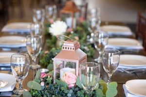 Elegant wedding table setting with lantern centerpiece surrounded by greenery and glassware.