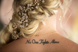 A close-up of a blonde braided hairstyle with crystal hair accessories and a tattoo visible on the back.