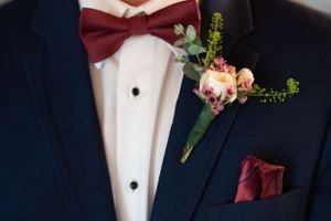 A detailed shot of a navy suit with burgundy bow tie and floral boutonniere.