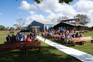 An outdoor wedding ceremony setup with wooden benches and white aisle runner under blue skies.