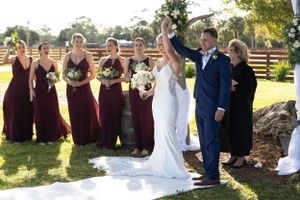 Wedding party with attendants in burgundy dresses celebrating on an outdoor white aisle.