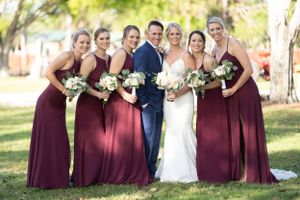 Wedding party in navy and burgundy attire posing together on sunny grounds.