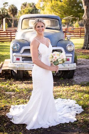White wedding gown in front of vintage blue pickup truck in rustic outdoor setting.