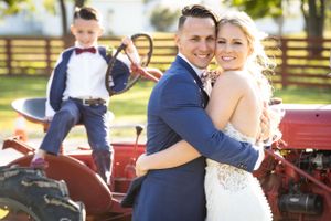 Rustic wedding portrait featuring vintage red tractor in background during outdoor celebration.