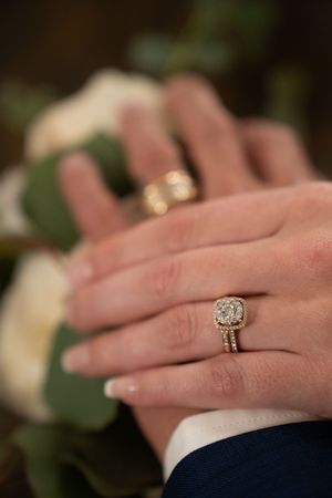 Close-up of elegant cushion-cut diamond engagement ring and wedding bands on intertwined hands.