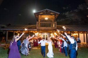 Wedding party celebrates with sparklers outside a rustic venue under moonlight.