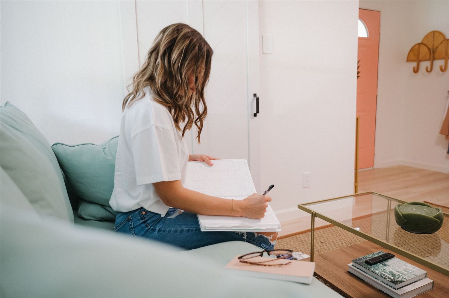 A person sits on a mint green couch writing in a notebook with modern decor.