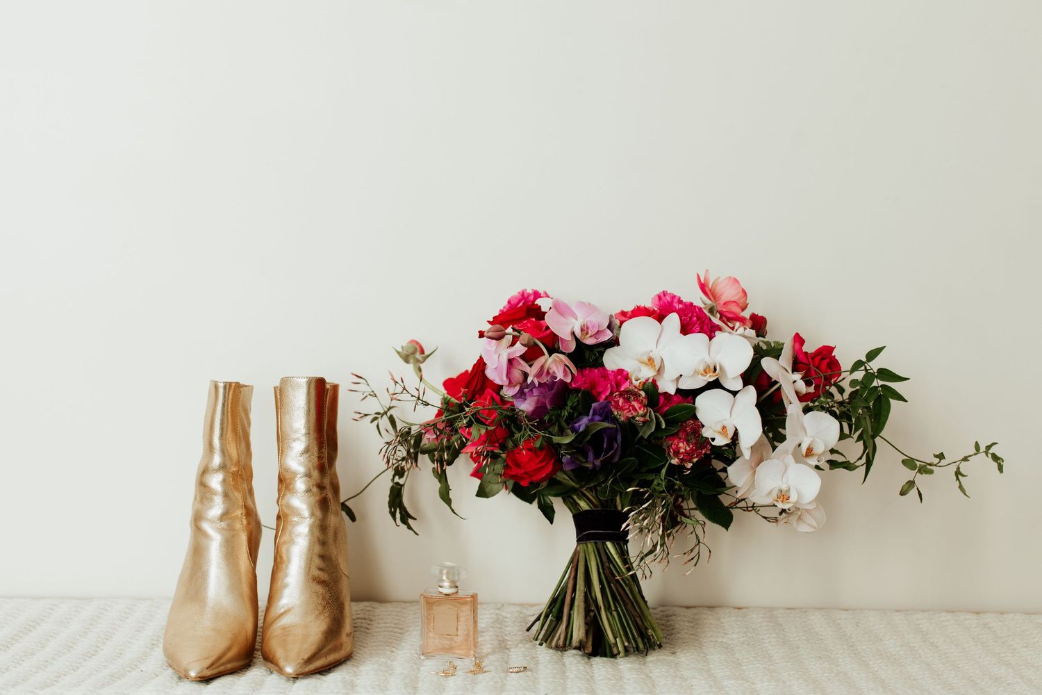 Gold boots and perfume bottle arranged with pink and white flower bouquet.