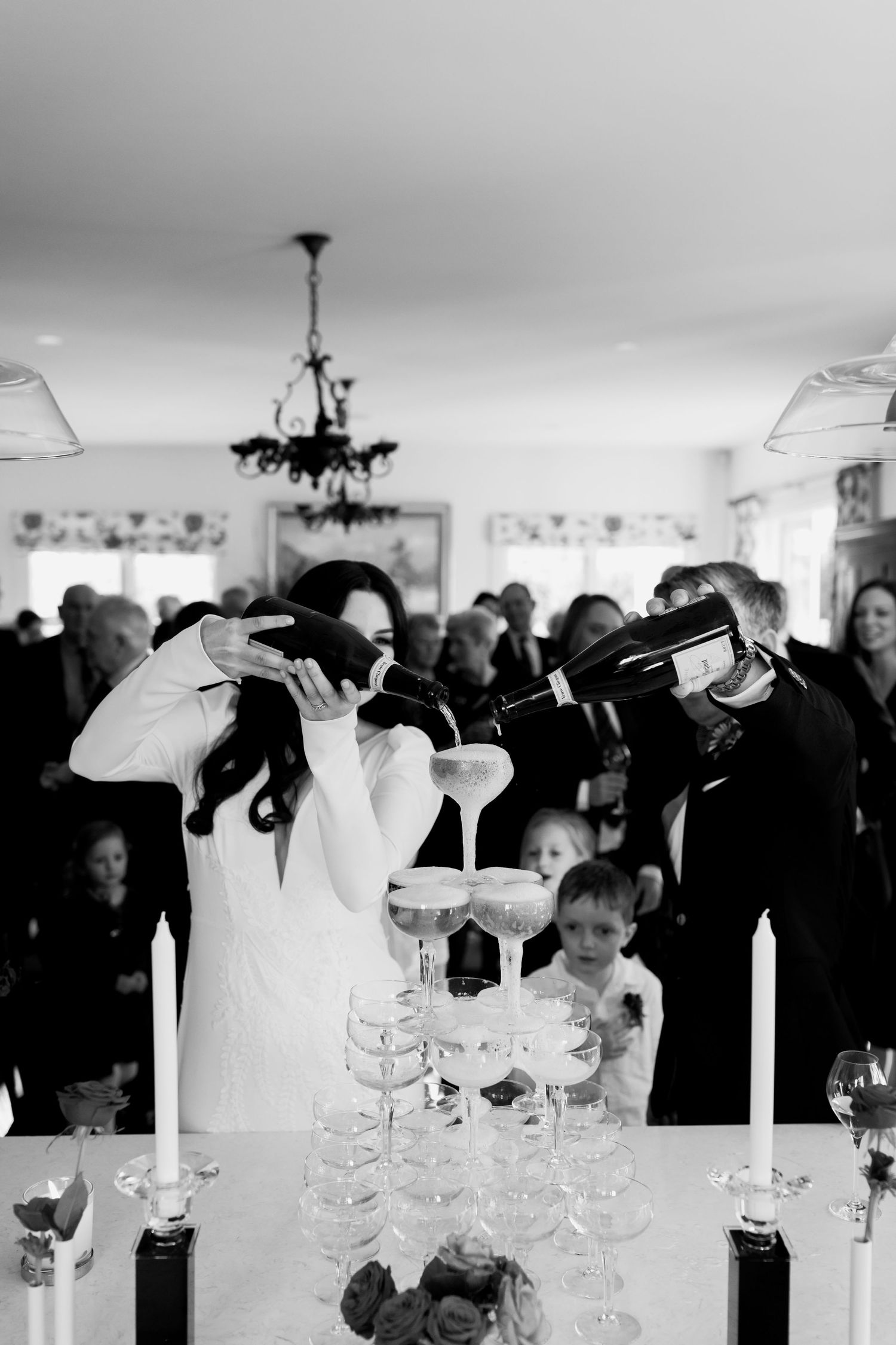 A dramatic black and white photo shows a champagne tower being filled at an indoor celebration.