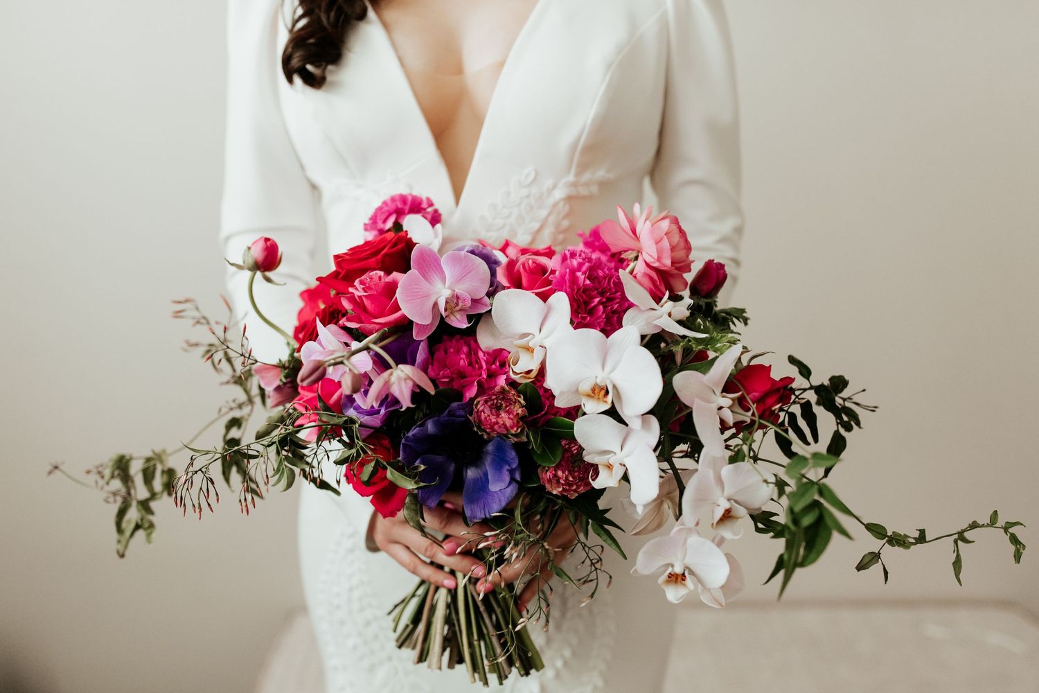 Stunning bridal bouquet with pink, purple, and white flowers with trailing greenery against white dress.