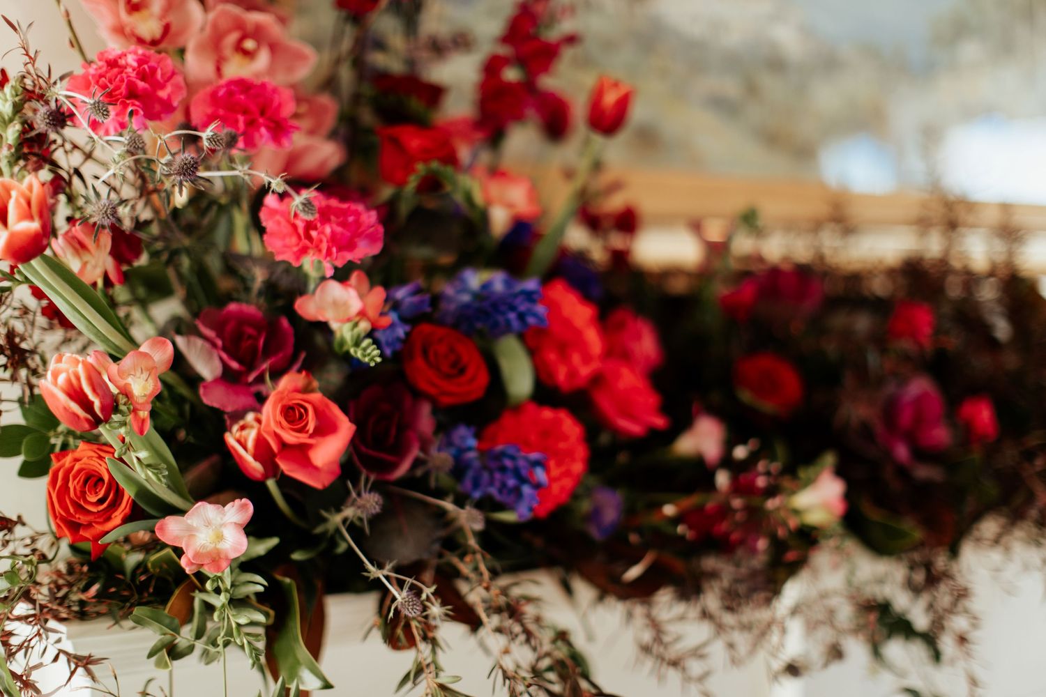 Lush floral arrangement featuring pink roses, red blooms and blue accents in a romantic wedding setting.