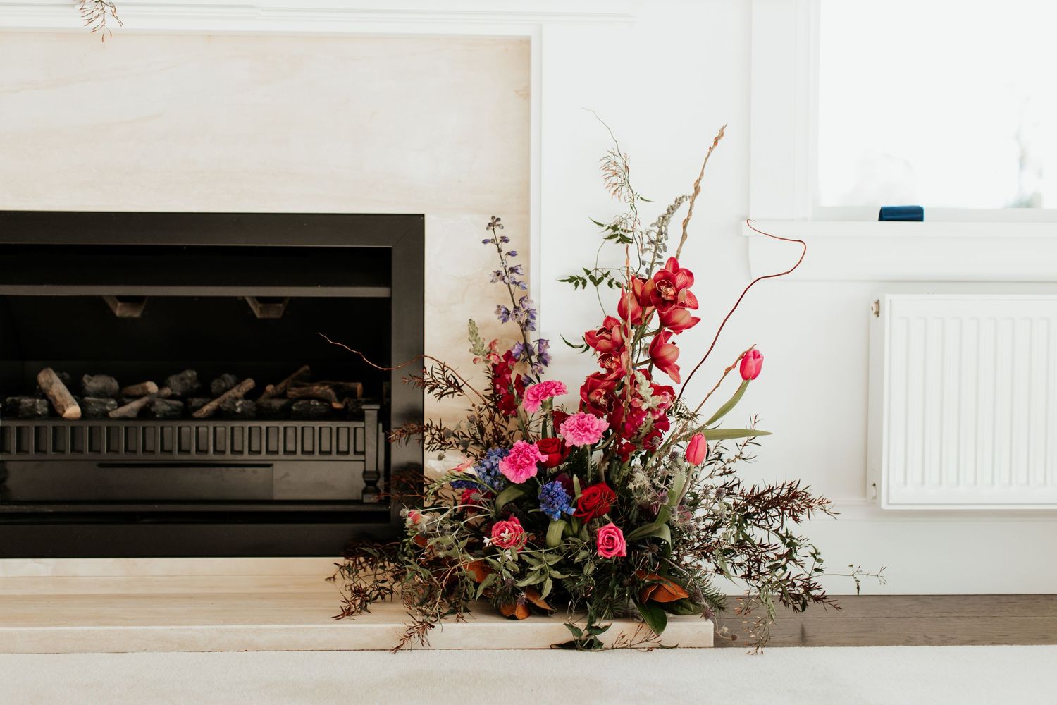 Vibrant pink and red floral arrangement displayed next to a modern fireplace in a bright white room.