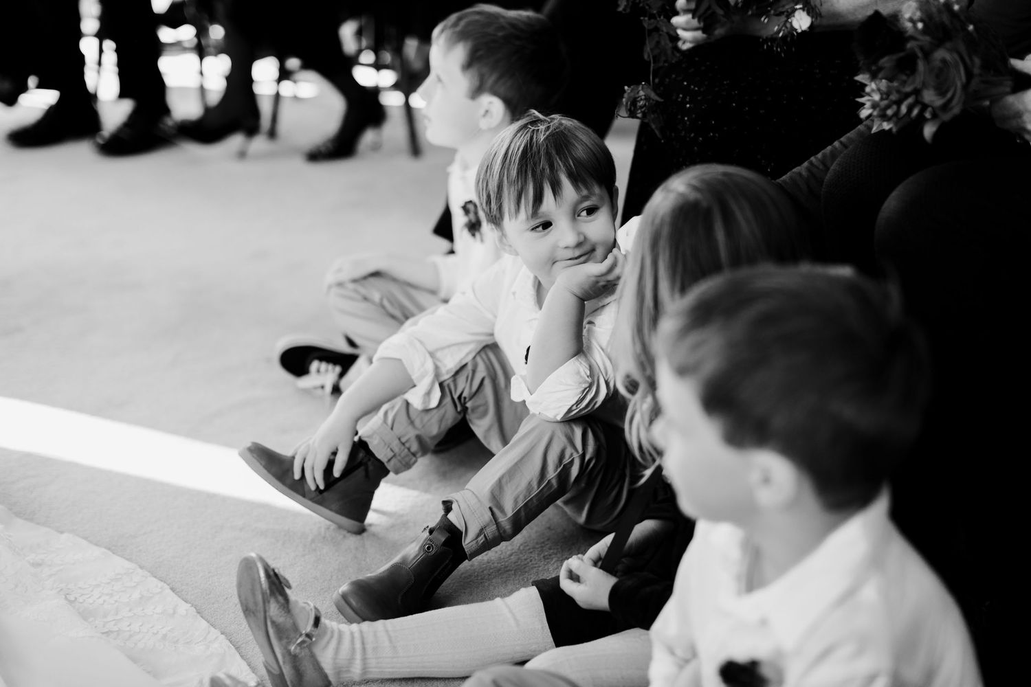Black and white photo of young children sitting and watching during a wedding celebration.