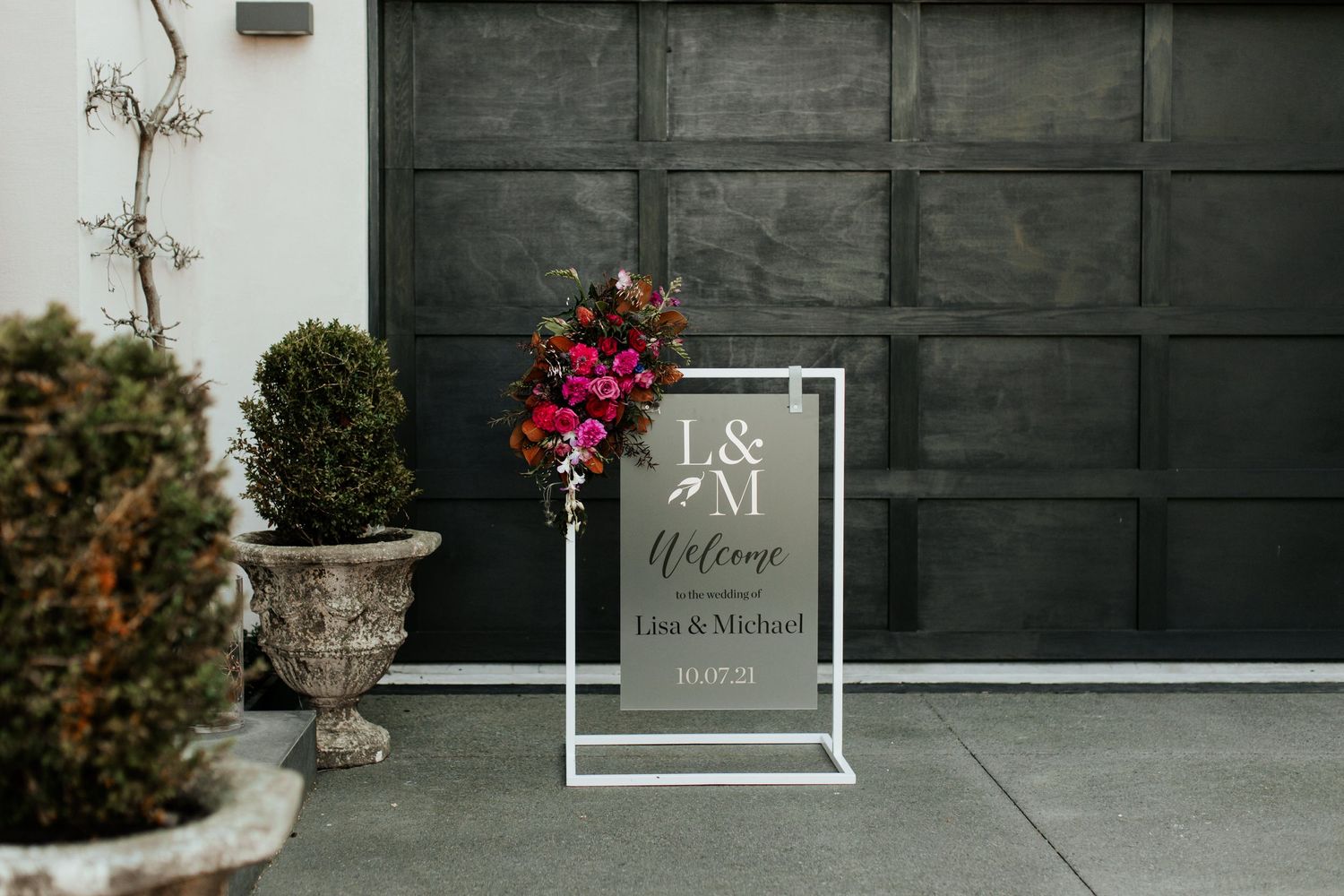 Modern welcome sign with floral accent displayed against dark garage door.