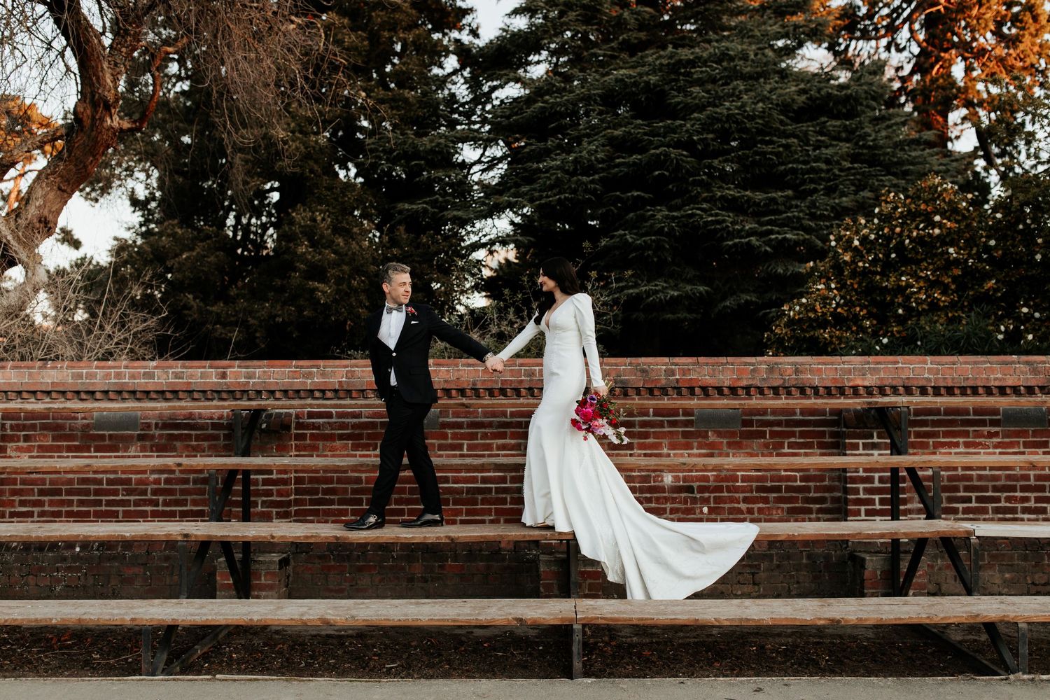 A couple in formal attire poses on brick stadium steps during autumn.