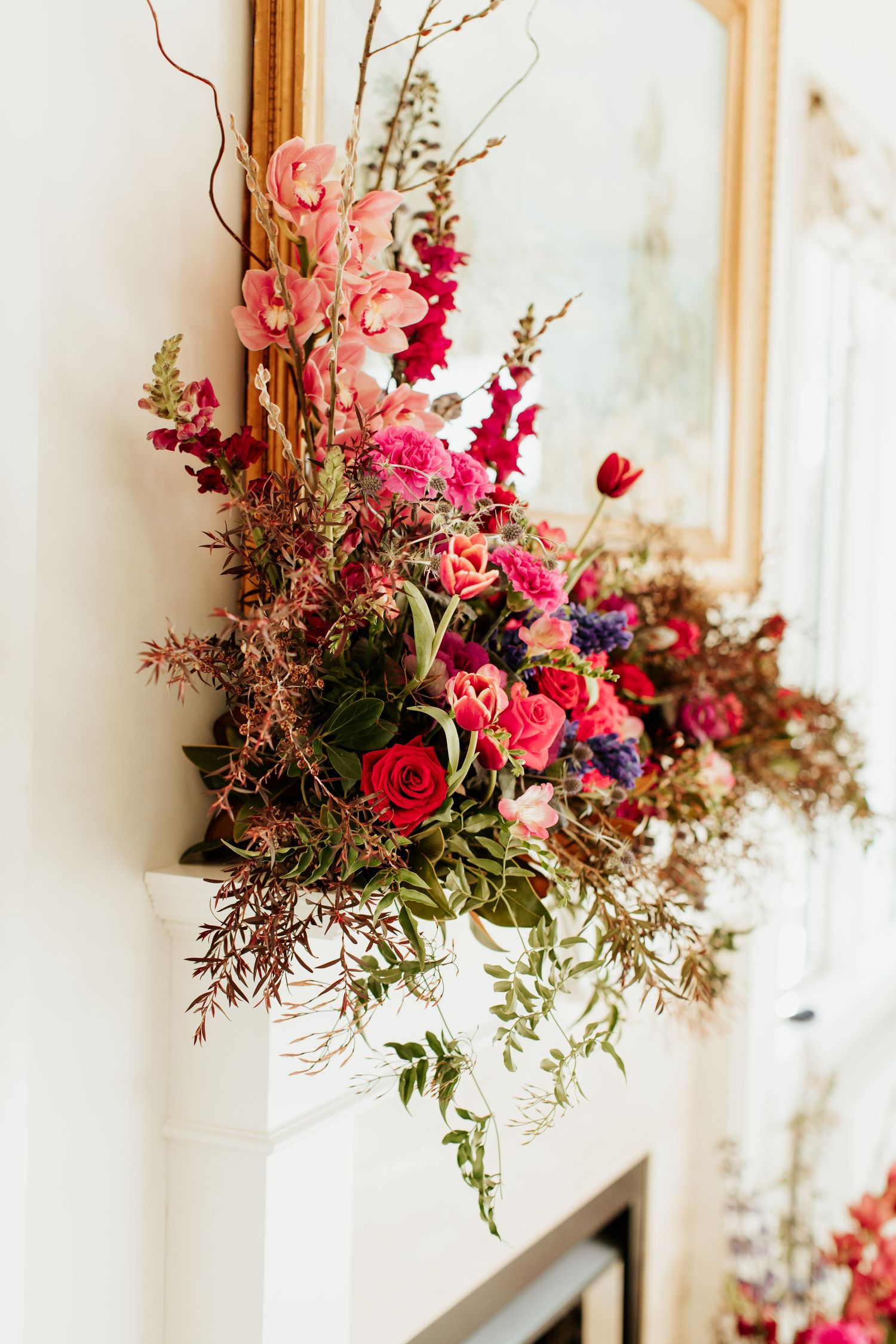 Elegant floral arrangement with pink roses and red blooms cascading over a white mantle.