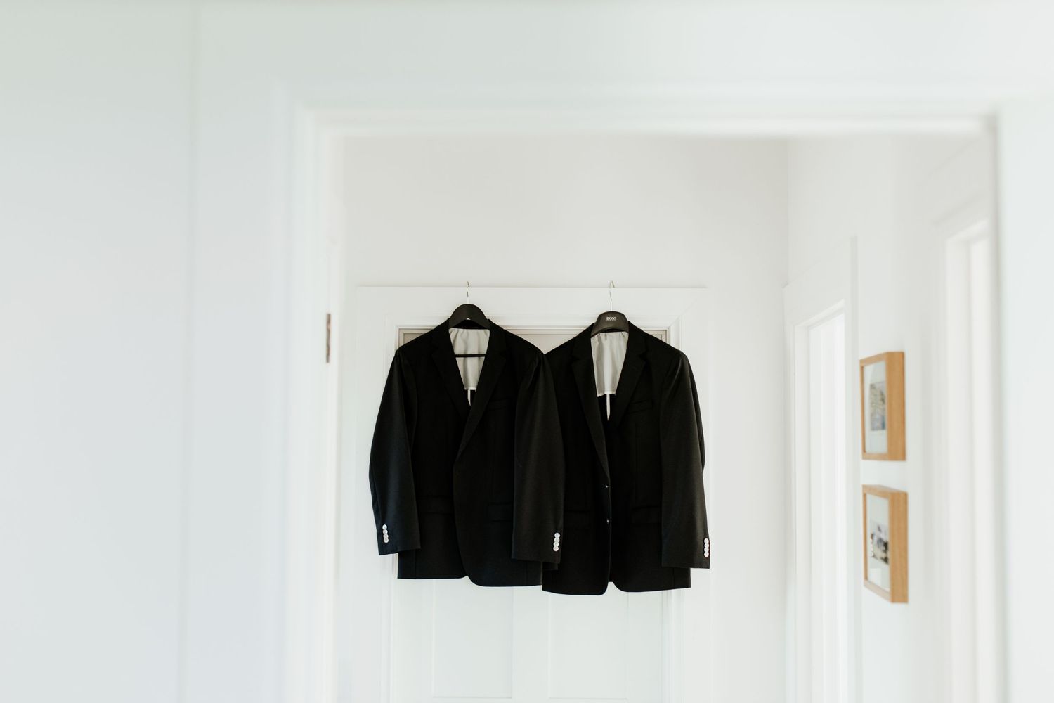 Two black suit jackets hanging on white wall in minimal setting.