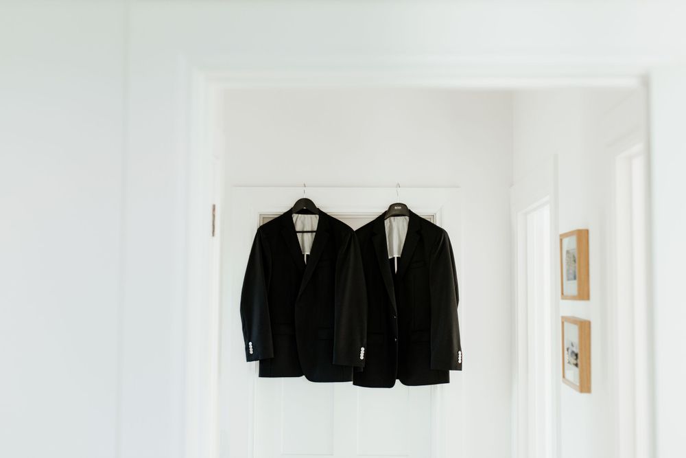 Two black suit jackets hanging on white wall in minimal setting.