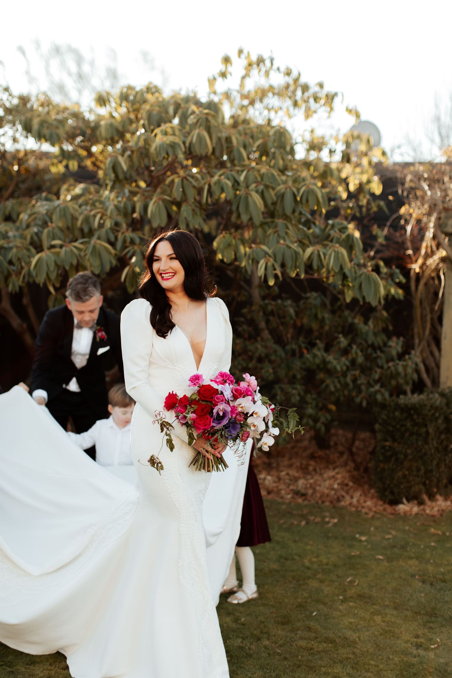 An autumn wedding scene shows flowing white dress and vibrant pink bouquet against foliage.