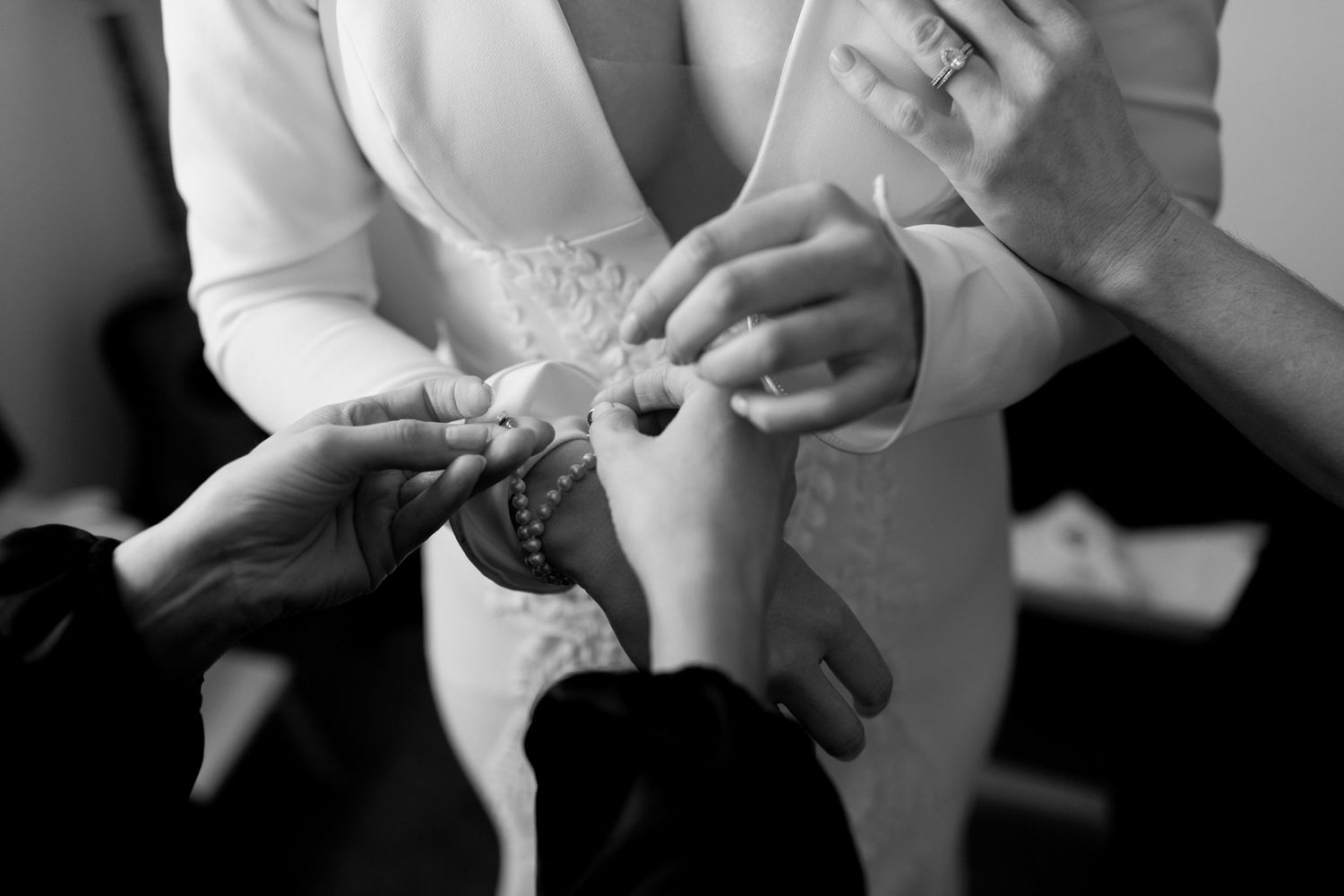 Close-up of hands adjusting jewelry during wedding preparation.
