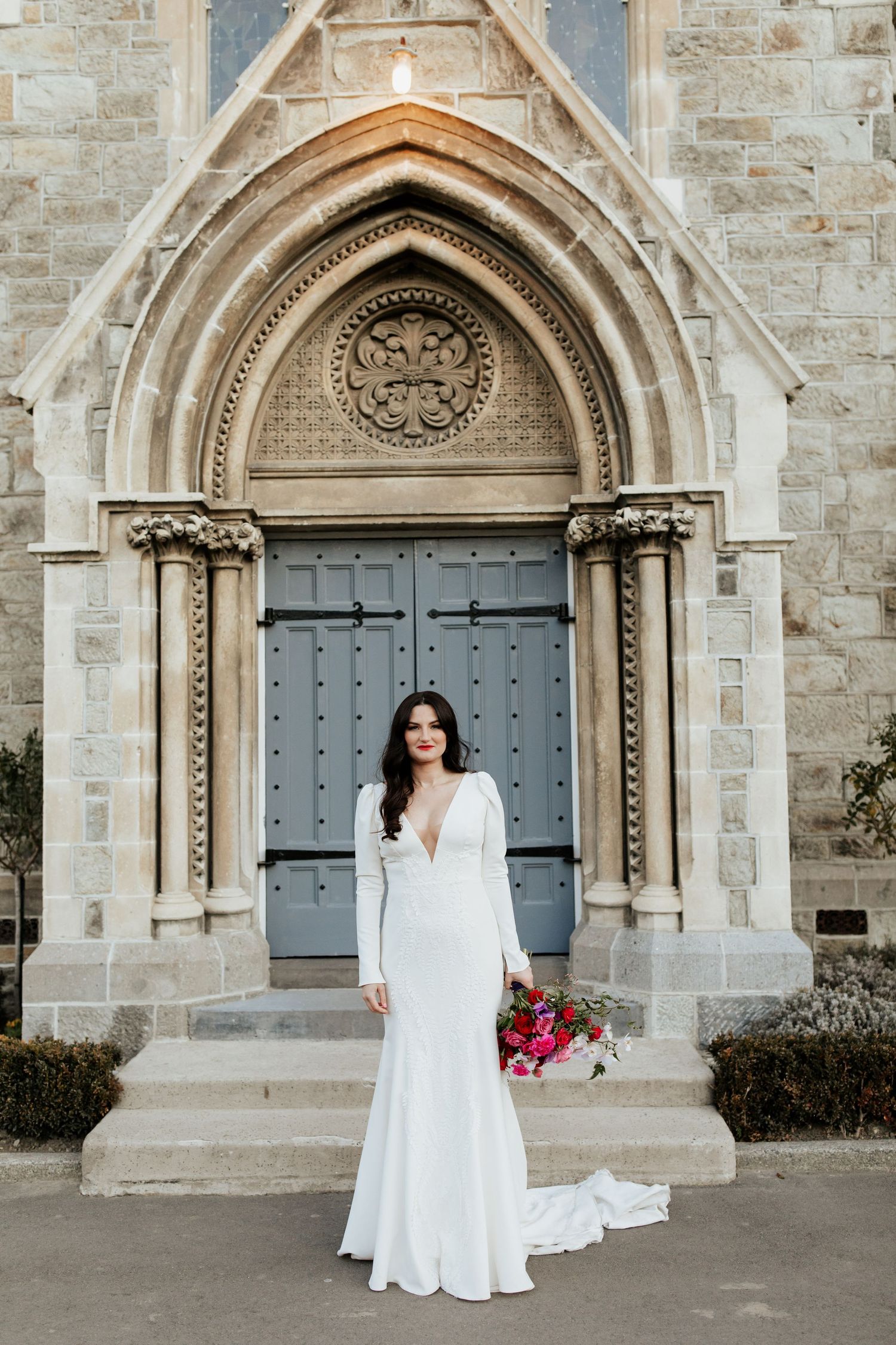 Elegant wedding dress with long sleeves and deep v-neck photographed in front of ornate gothic church doorway.