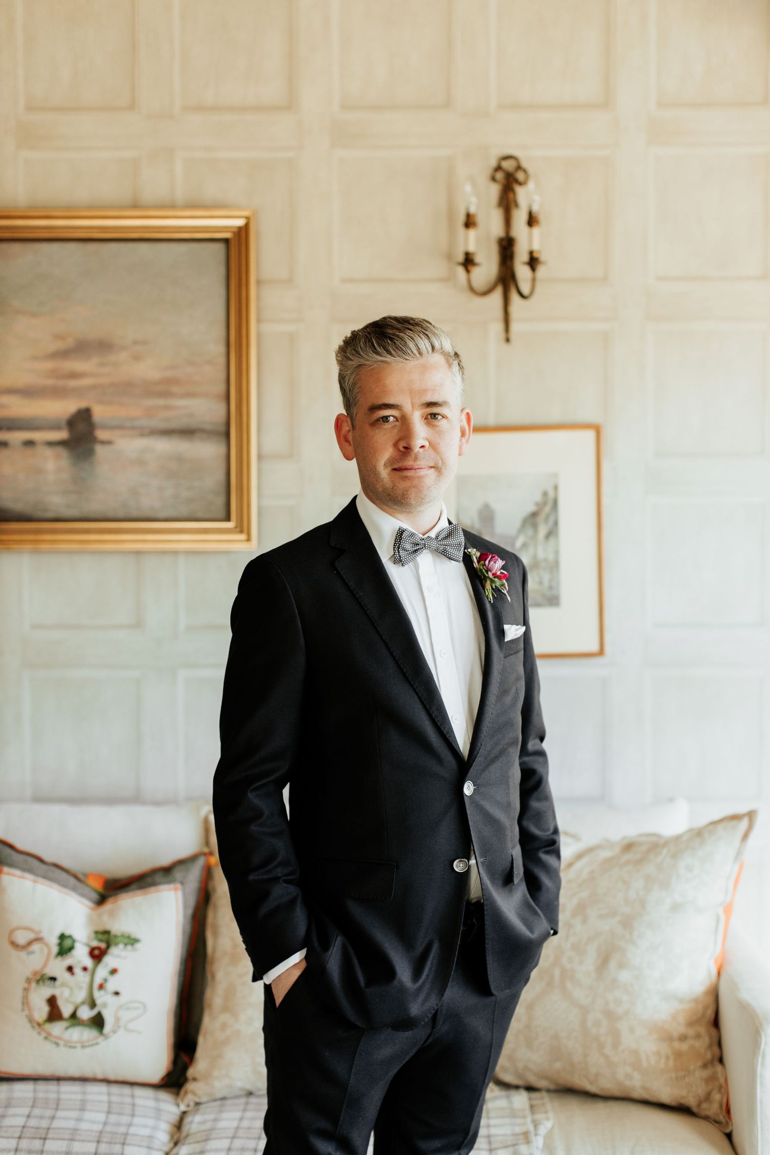 Formal attire with bow tie and boutonniere against white paneled wall.
