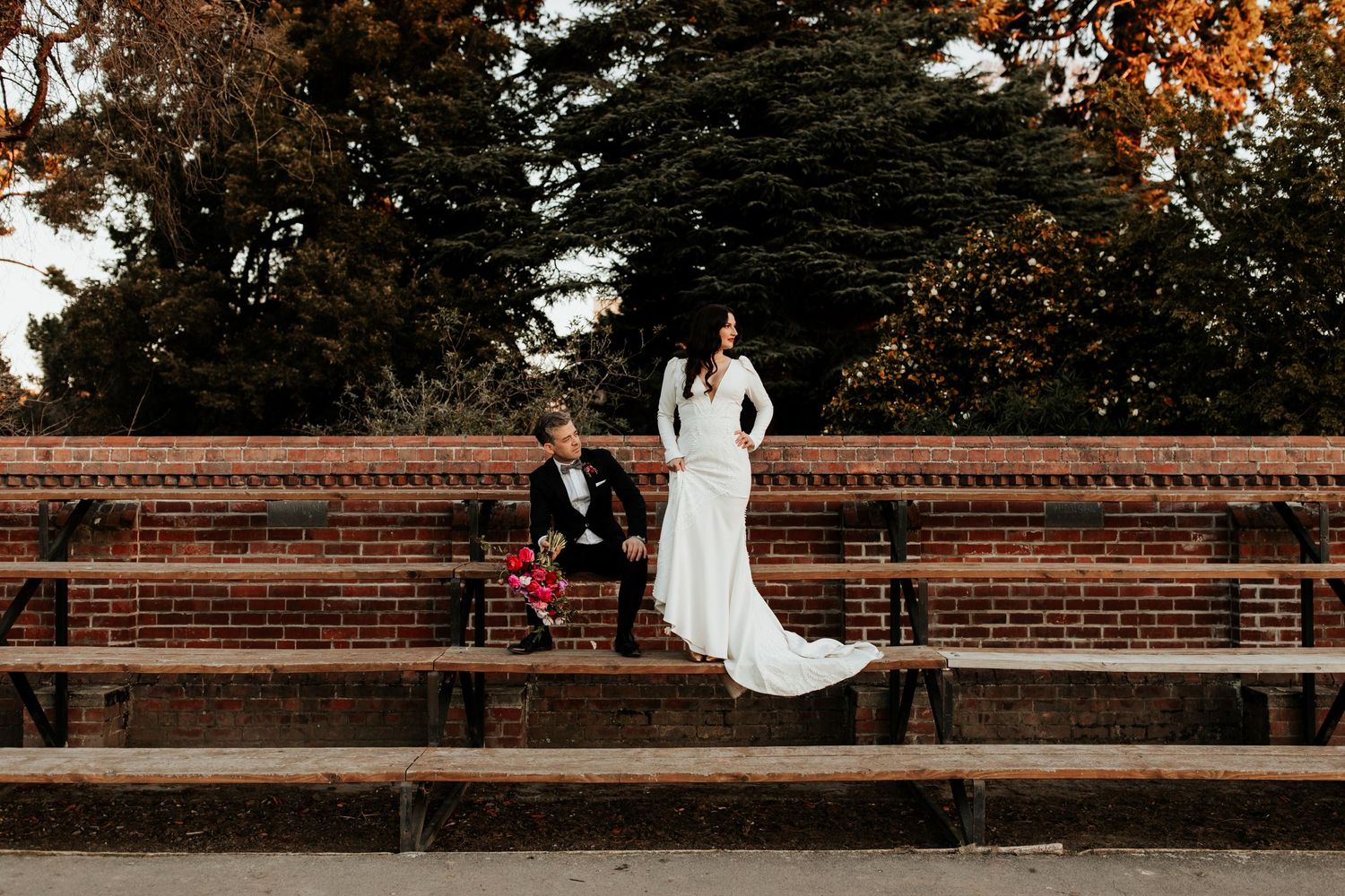 A couple sits on brick amphitheater steps surrounded by autumn trees.