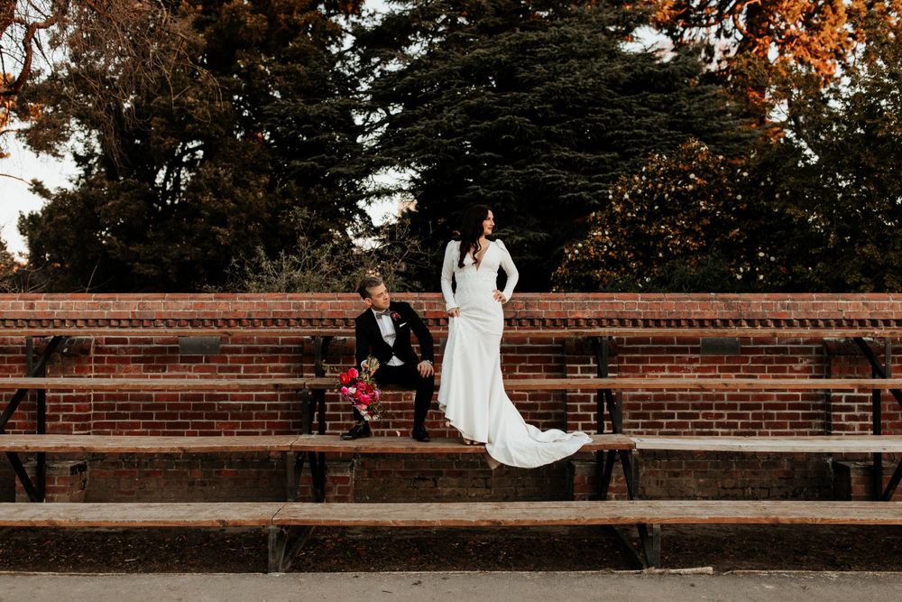A couple sits on brick amphitheater steps surrounded by autumn trees.